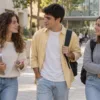 Tres jóvenes con mochilas y apuntes conversan en un campus universitario